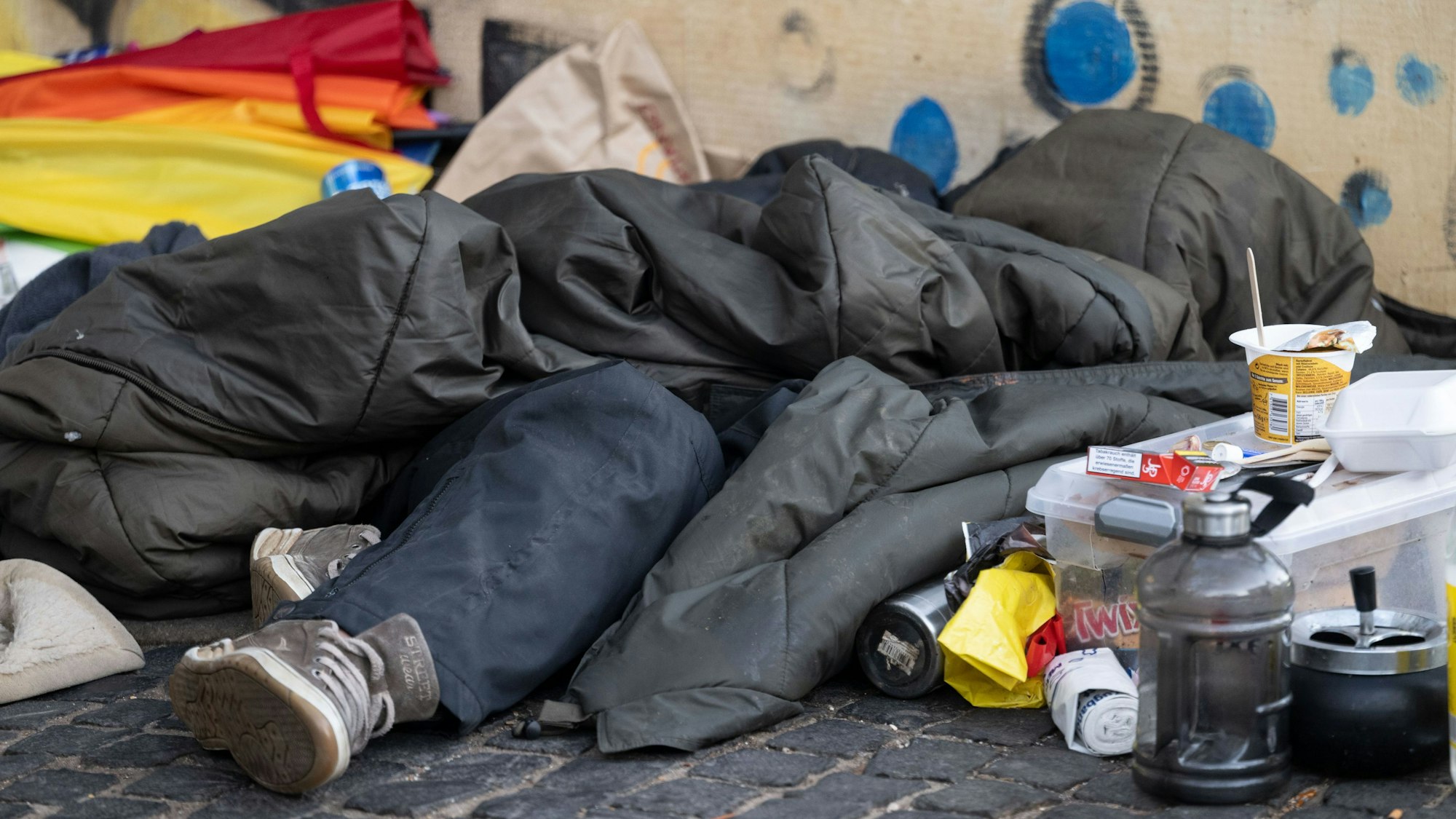 Eine Person liegt in der Innenstadt unter einem Schlafsack.