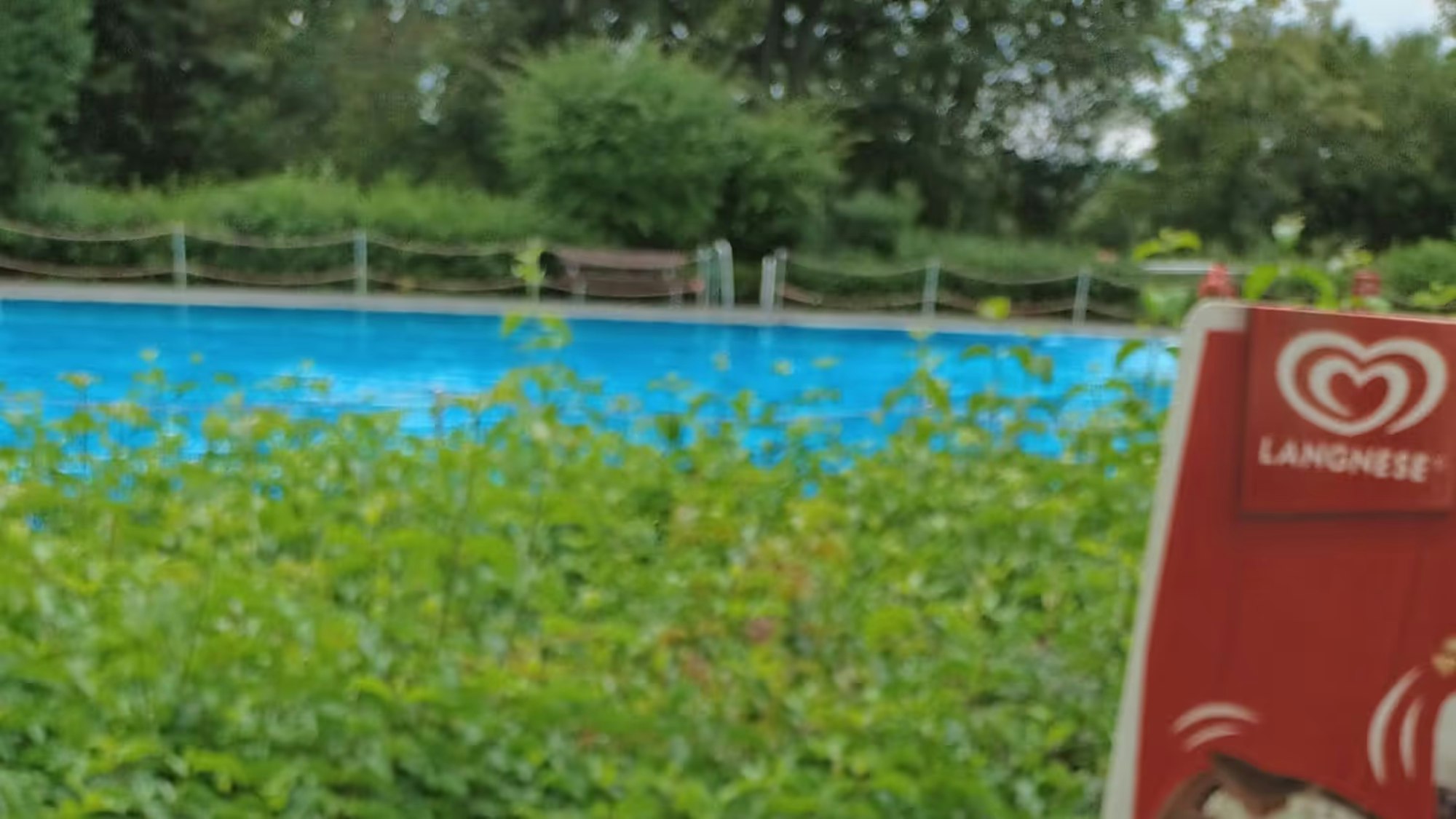 Pommes Frites mit Ketchup, im Hintergrund Werbung für Eis und ein Schwimmbecken.