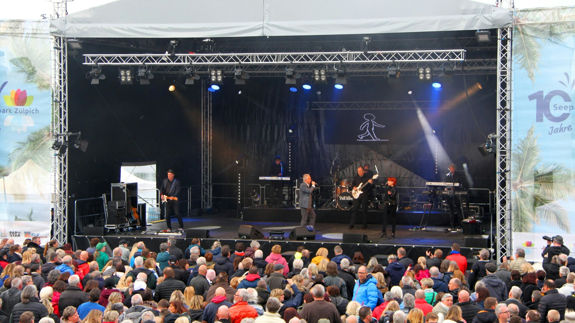 Vor der überdachten Bühne stehen zahlreiche Zuschauerinnen und Zuschauer.