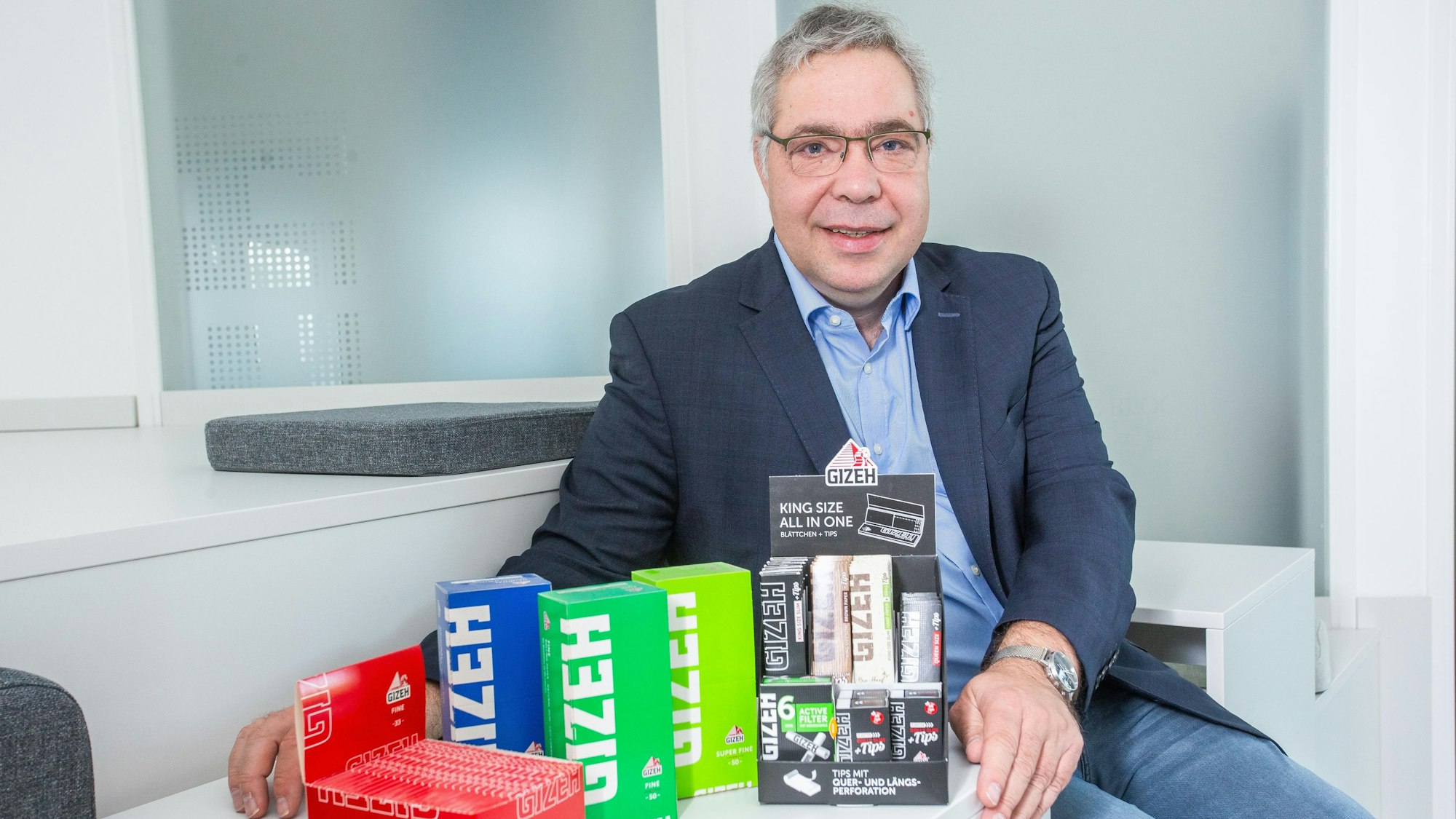 Ein Mann sitzt vor einer Reihe von bunten Schachteln.