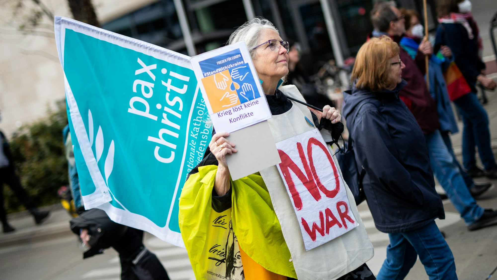 Eine Ostermarsch-Teilnehmerin in Stuttgart hält eine Fahne von „Pax Christi“ und trägt ein Anti-Kriegs-Transparent.