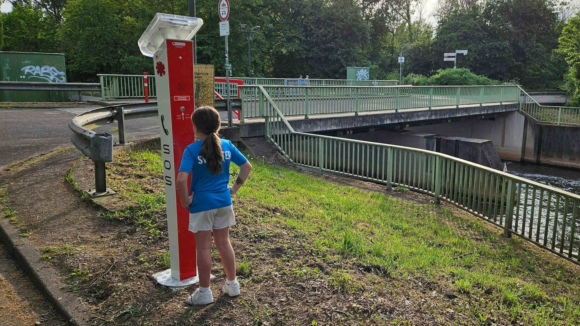Das Bild zeigt eine Notrufsäule an der Erft mit einem Kind.