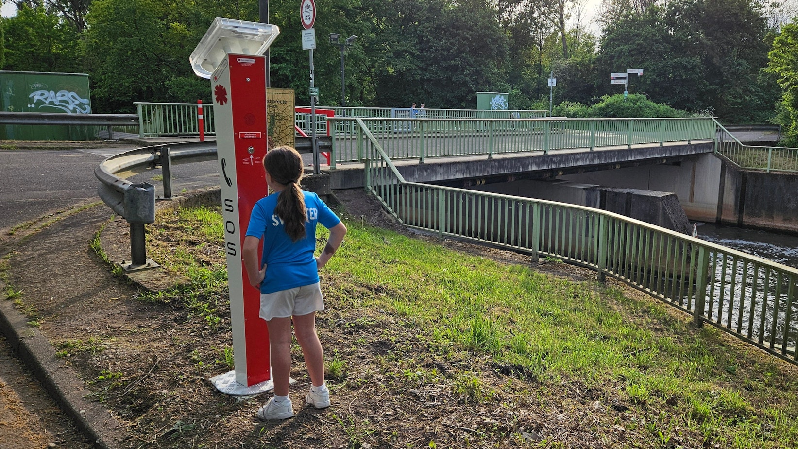 Das Bild zeigt eine Notrufsäule an der Erft mit einem Kind.