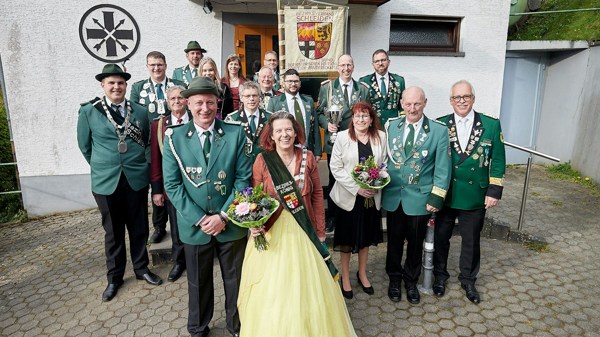 Claudia Stern steht im gelben Ballkleid und mit Schärpe auf einem Platz, umringt von einigen Schützenvereinsmitgliedern in Uniform.