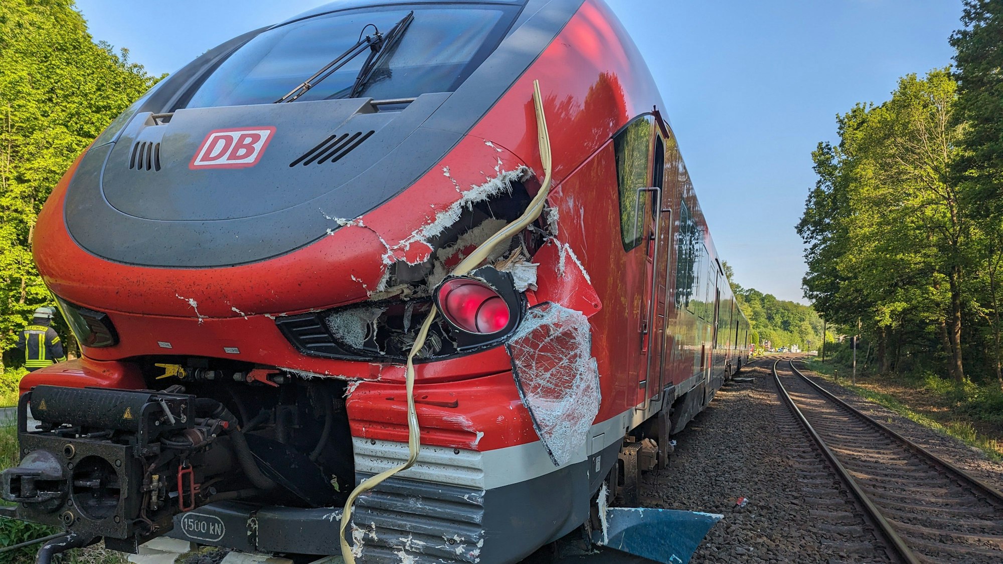 Eine Bahn, die an ihrer Front beschädigt wurde, steht auf Schienen. In der Umgebung stehen Bäume.