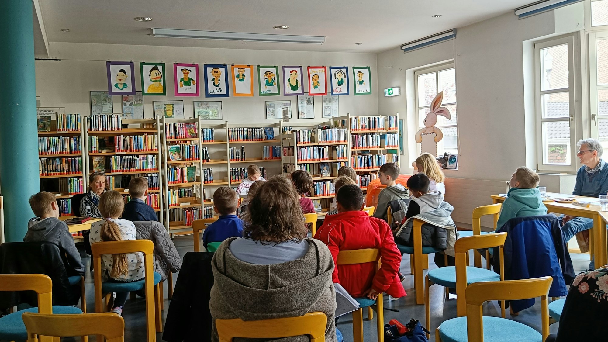 Ein Raum ist gefüllt mit Stühlen, auf denen Kinder und Erwachsene sitzen.