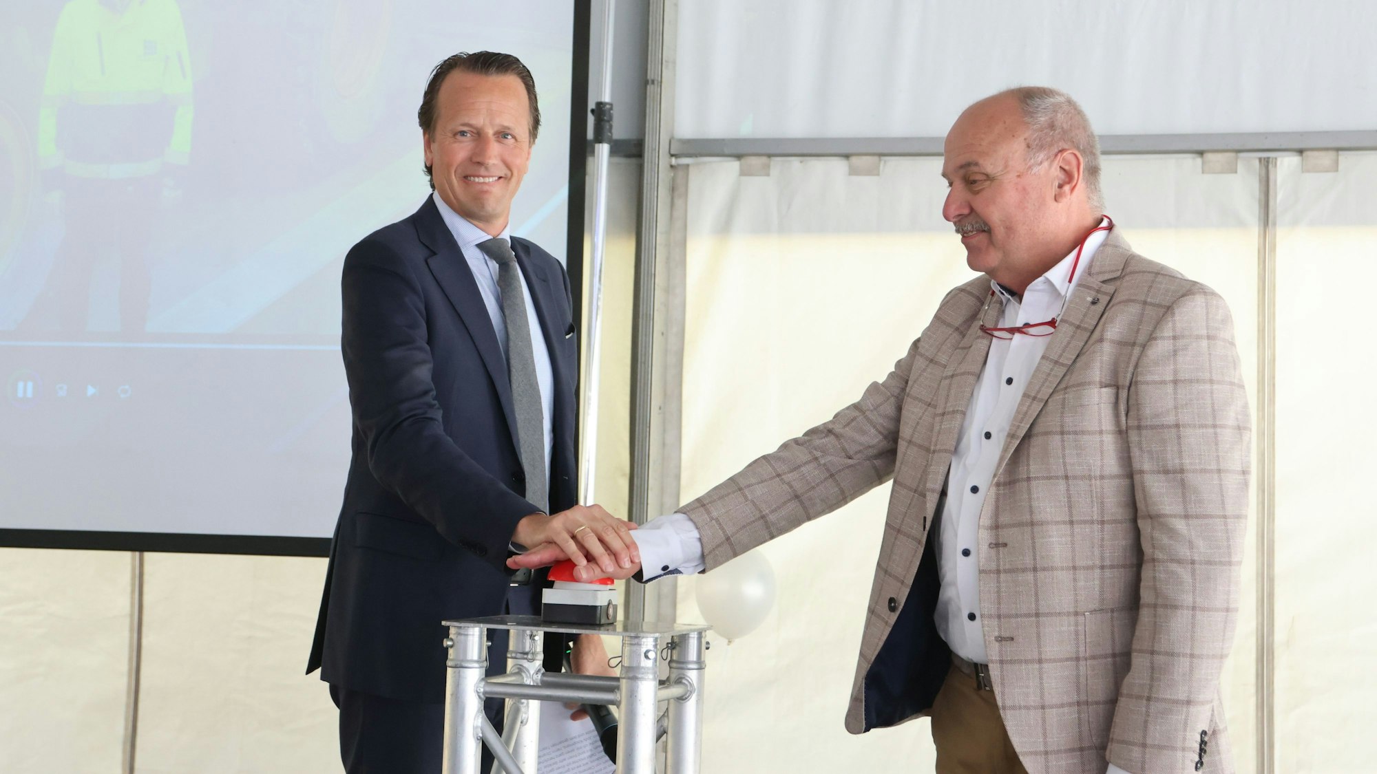 Zwei Männer drücken gemeinsam auf einen Startknopf.