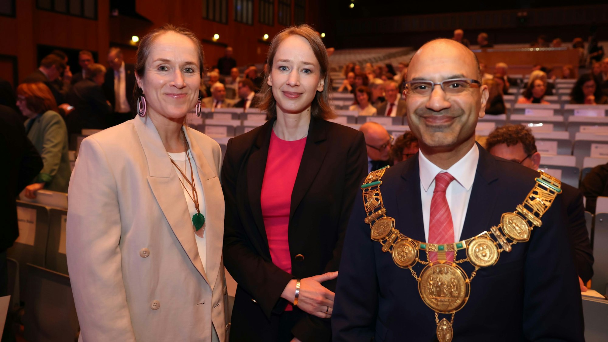 Der Rektor der Universität mit seiner Ehrenkette und zwei Frauen in einem Hörsaal.