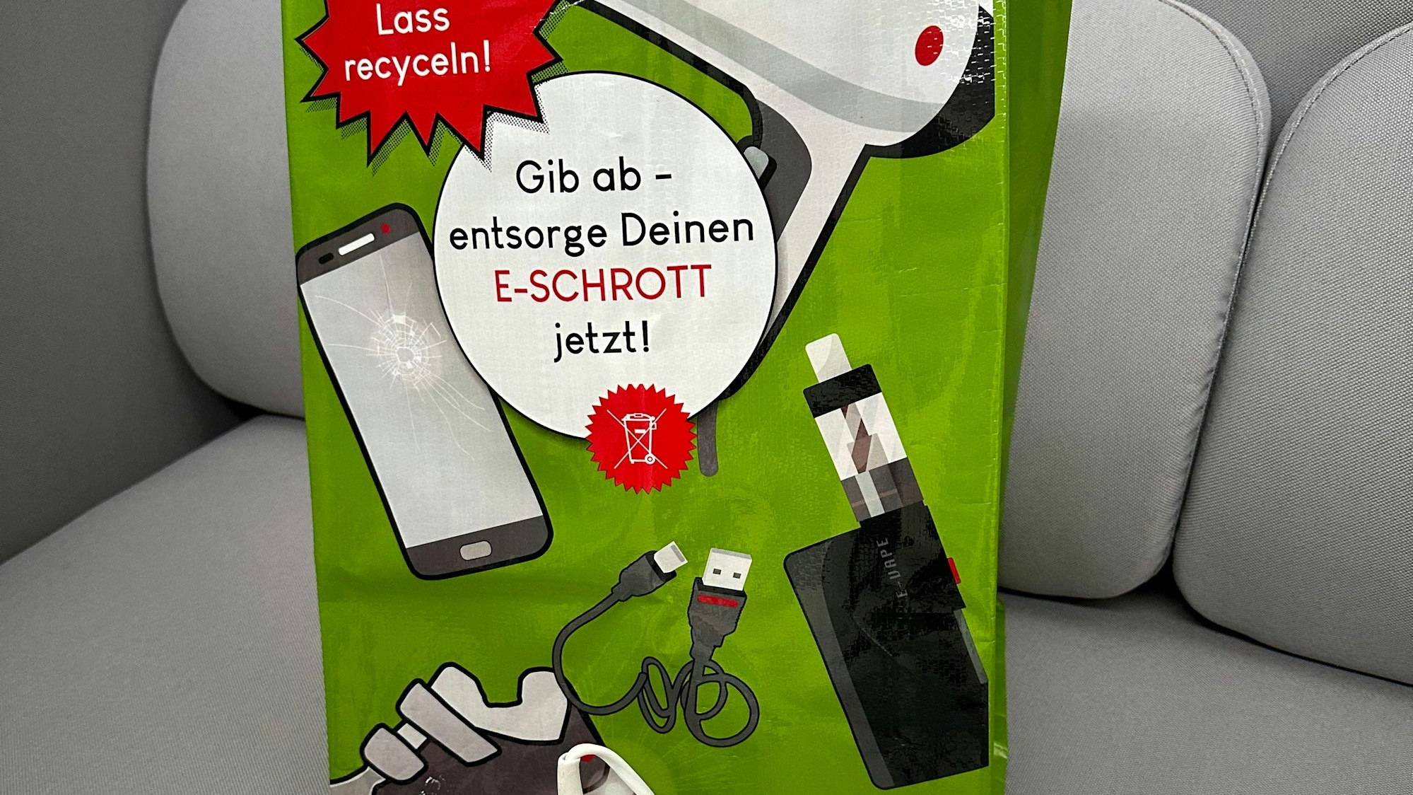 Vor einer grünen Tasche liegen kleine Elektrogeräte.