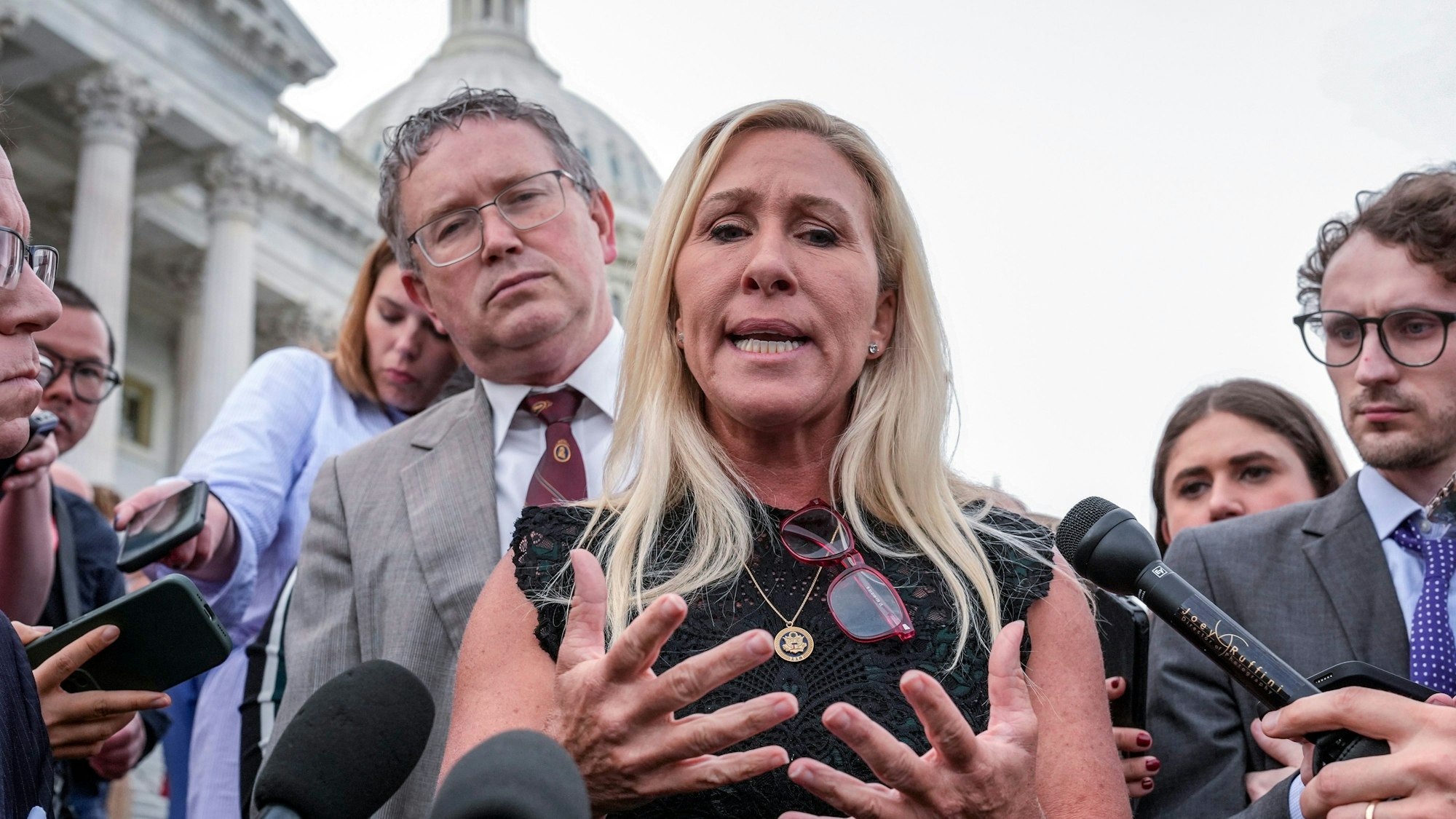 Es ist die Abgeordnete Marjorie Taylor Greene zu sehen, wie sie vor Reportern in Mikros spricht.