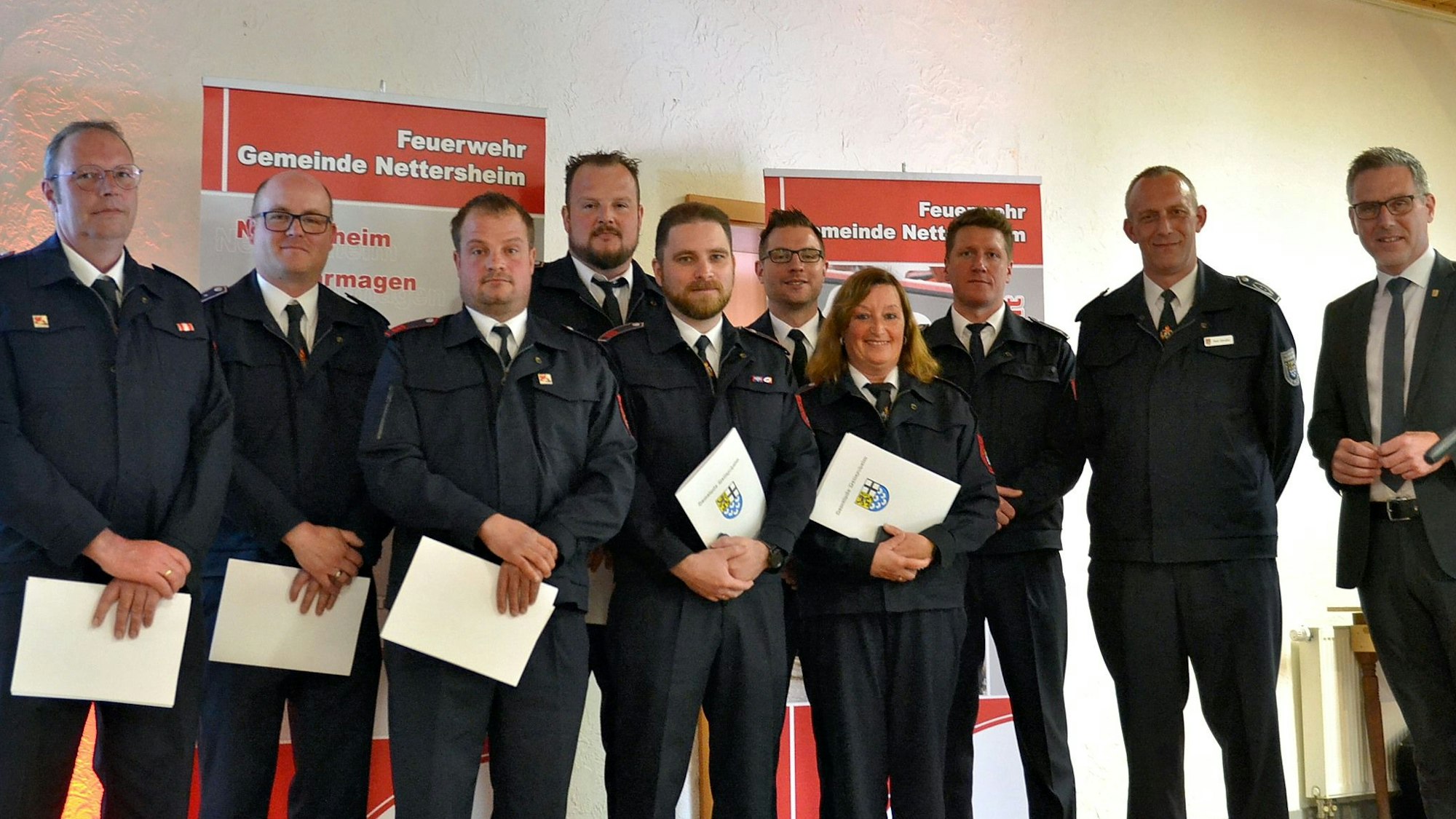Zahlreiche Feuerwehrleute aus Nettersheim halten Urkunden mit dem Gemeindewappen in den Händen. Rechts steht Bürgermeister Norbert Crump.
