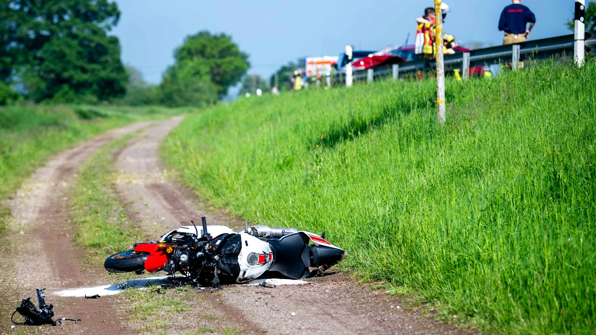 Ein Motorrad liegt nach einem schweren Unfall auf einem Feldweg. Rechts oberhalb ist die Landstraße bei Euskirchen zu sehen, wo sich der Unfall ereignete.