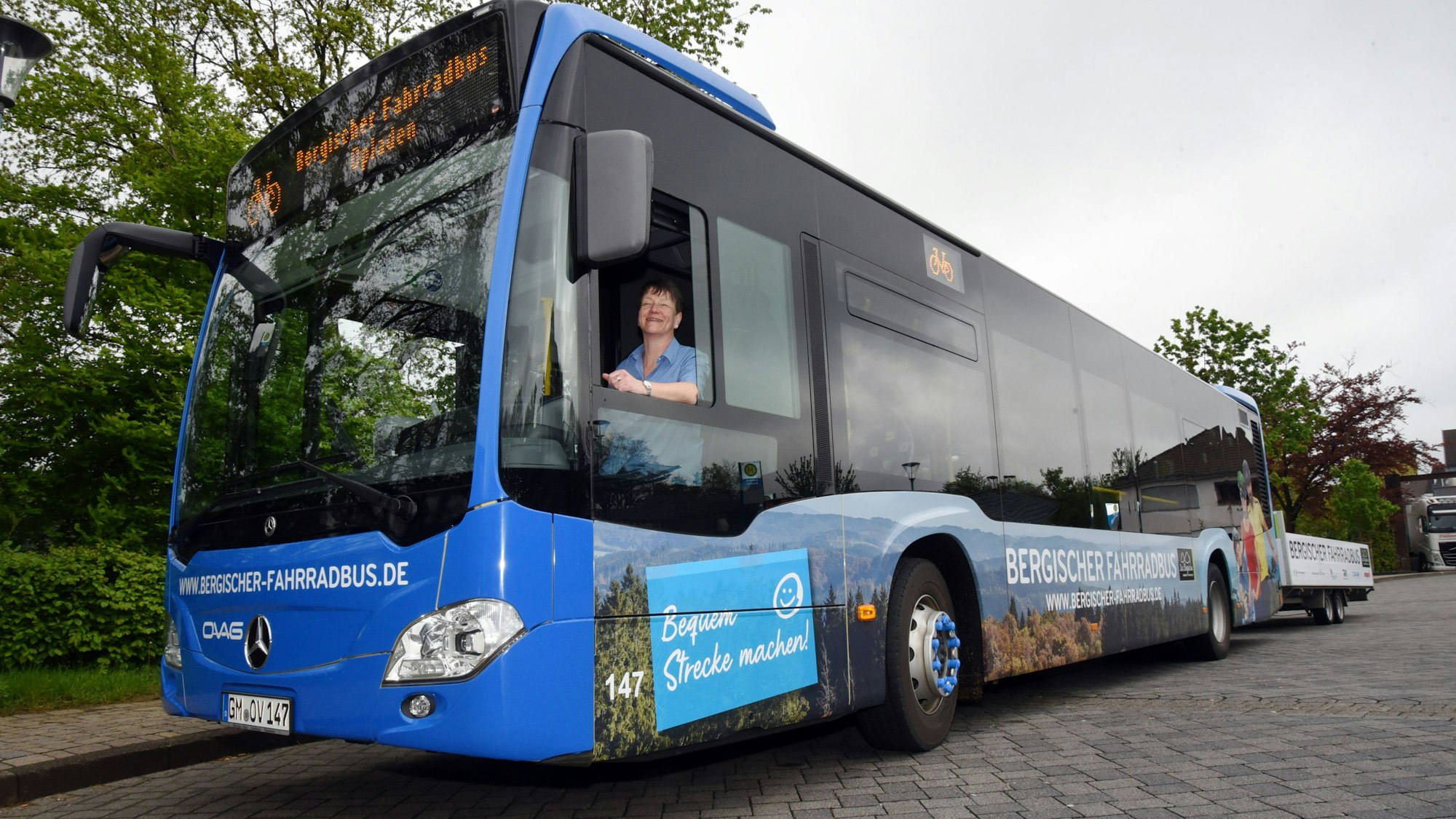 Eine Frau sitzt am Steuer eines Busses der Ovag und lacht aus dem geöffneten Fahrerfenster.