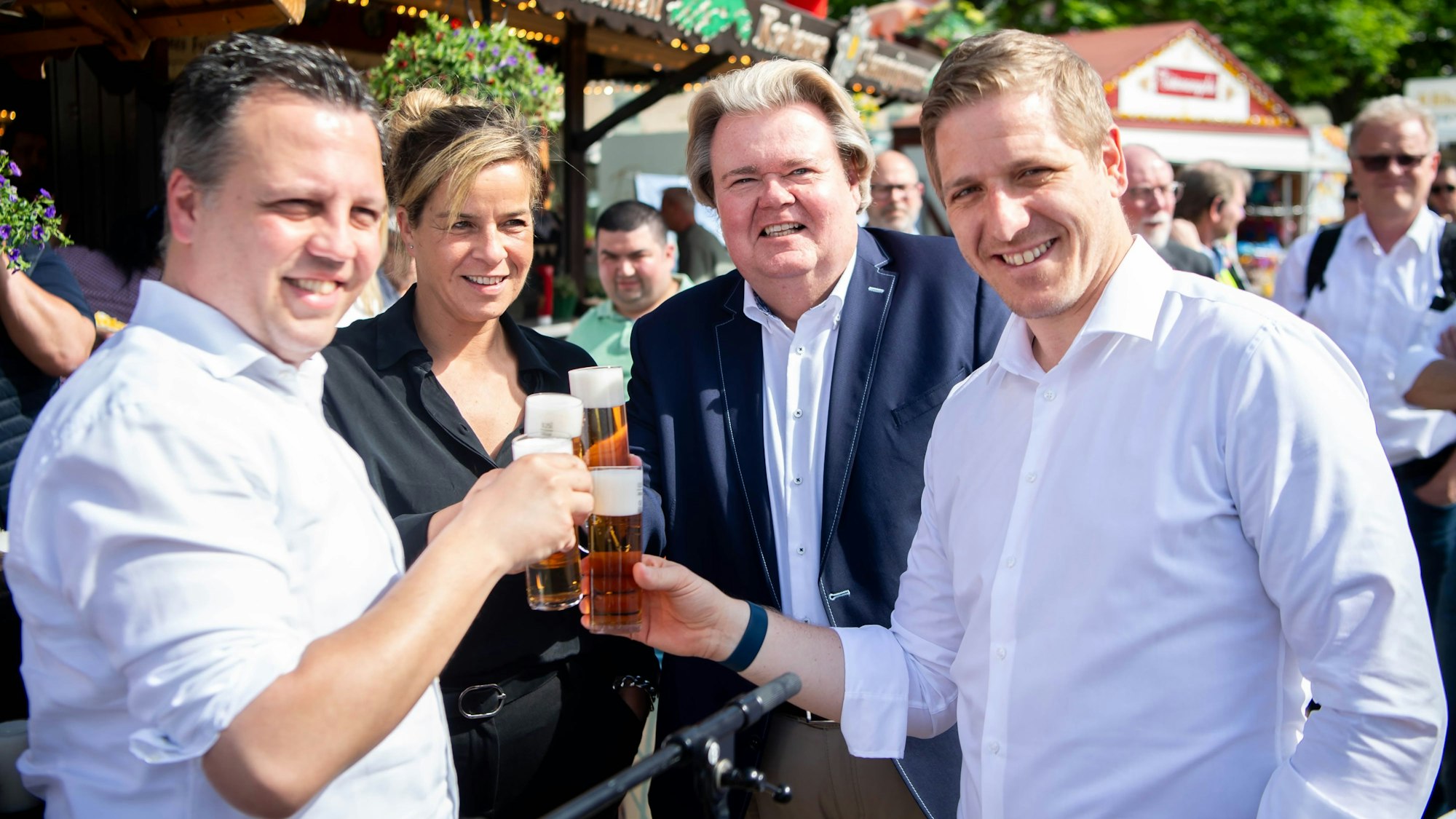 Sache Reichelt, Mona Neubaur, Klaus Voussem und Markus Ramers halten ein Kölsch in der Hand.