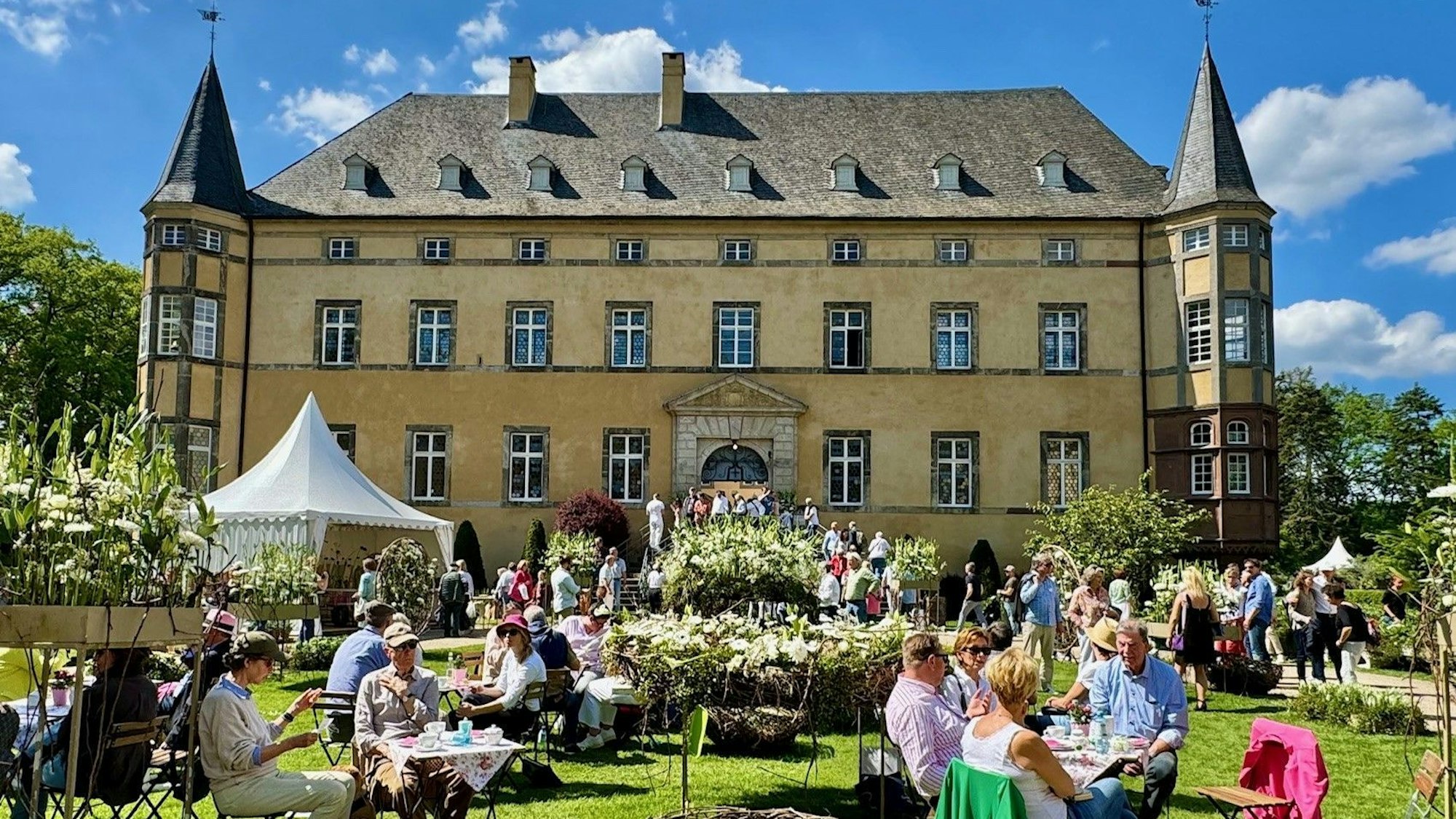 Wachtberg-Adendorf, Menschen sitzen an Tischen im schön dekorierten 
Burggarten.