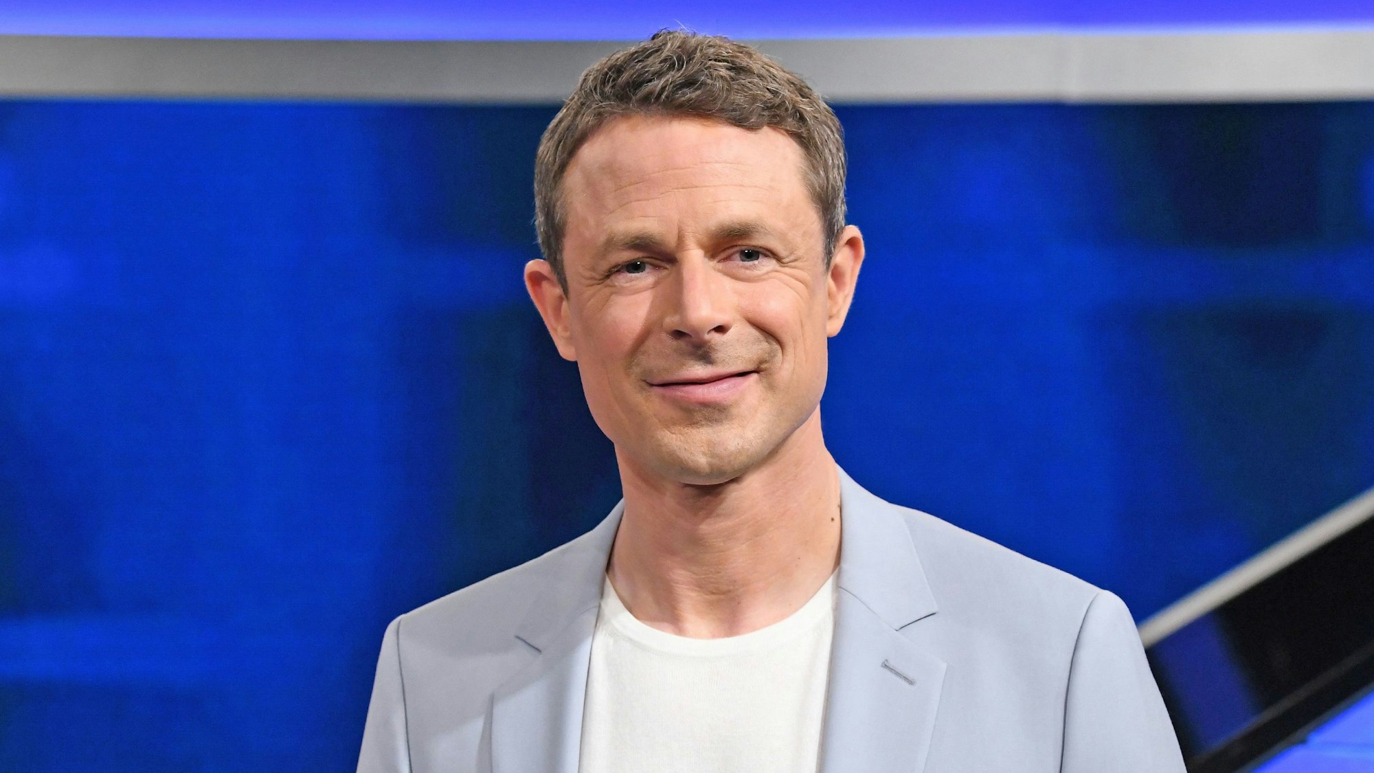 Moderator Alexander Bommes steht im Studio der ARD-Quizshow „Gefragt – Gejagt“ und lächelt in die Kamera.