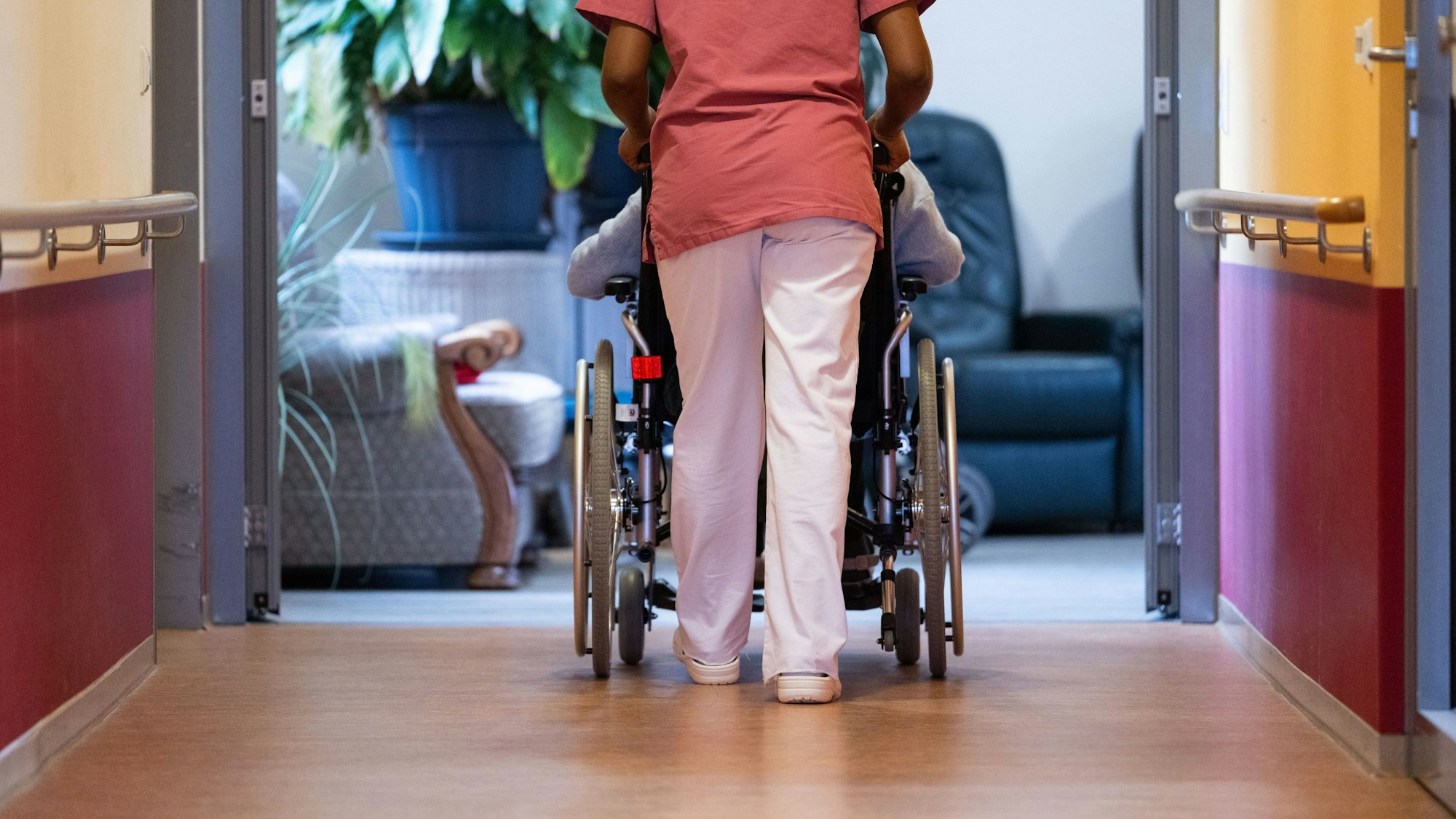 ARCHIV - 07.02.2024, Baden-Württemberg, Filderstadt: Eine Bewohnerin eines Pflegeheims wird von einer Pflegerin einen Gang entlang geschoben.