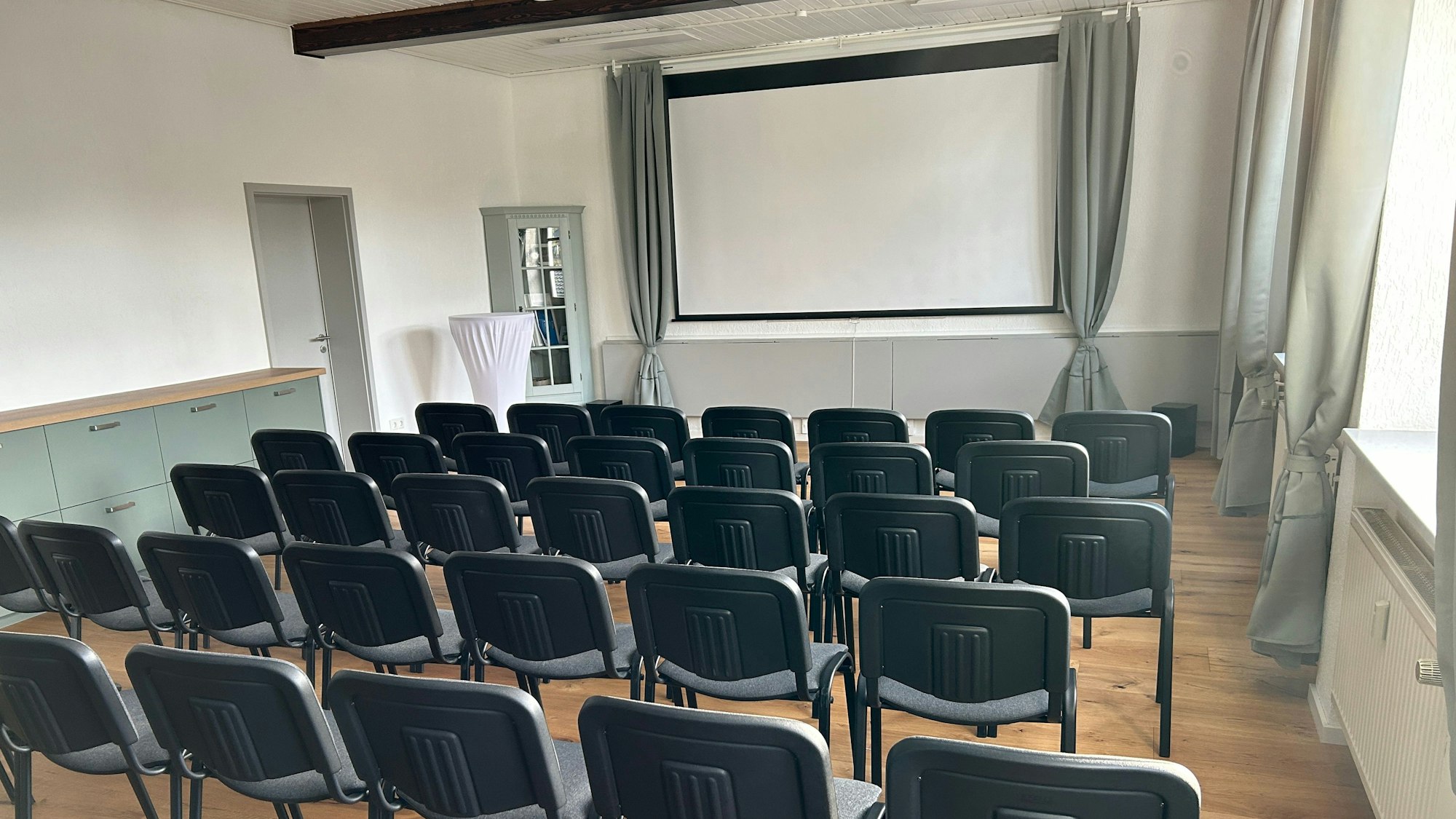 Im Saal stehen Stuhlreihen vor einer Leinwand.
