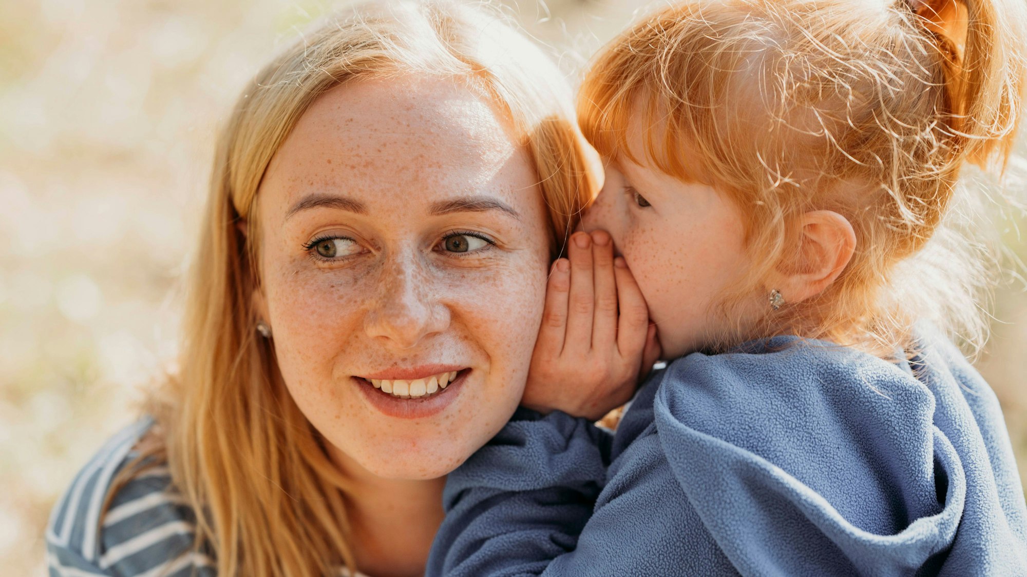 Junges Kind flüstert einer Frau etwas ins Ohr