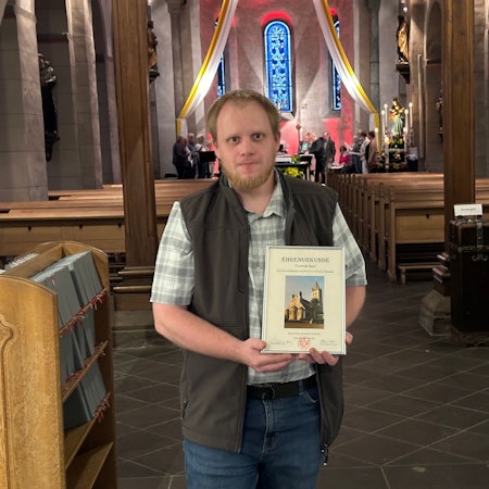 Foto von Dominik Beul in einem Kirchenraum – mit Urkunde in den Händen.