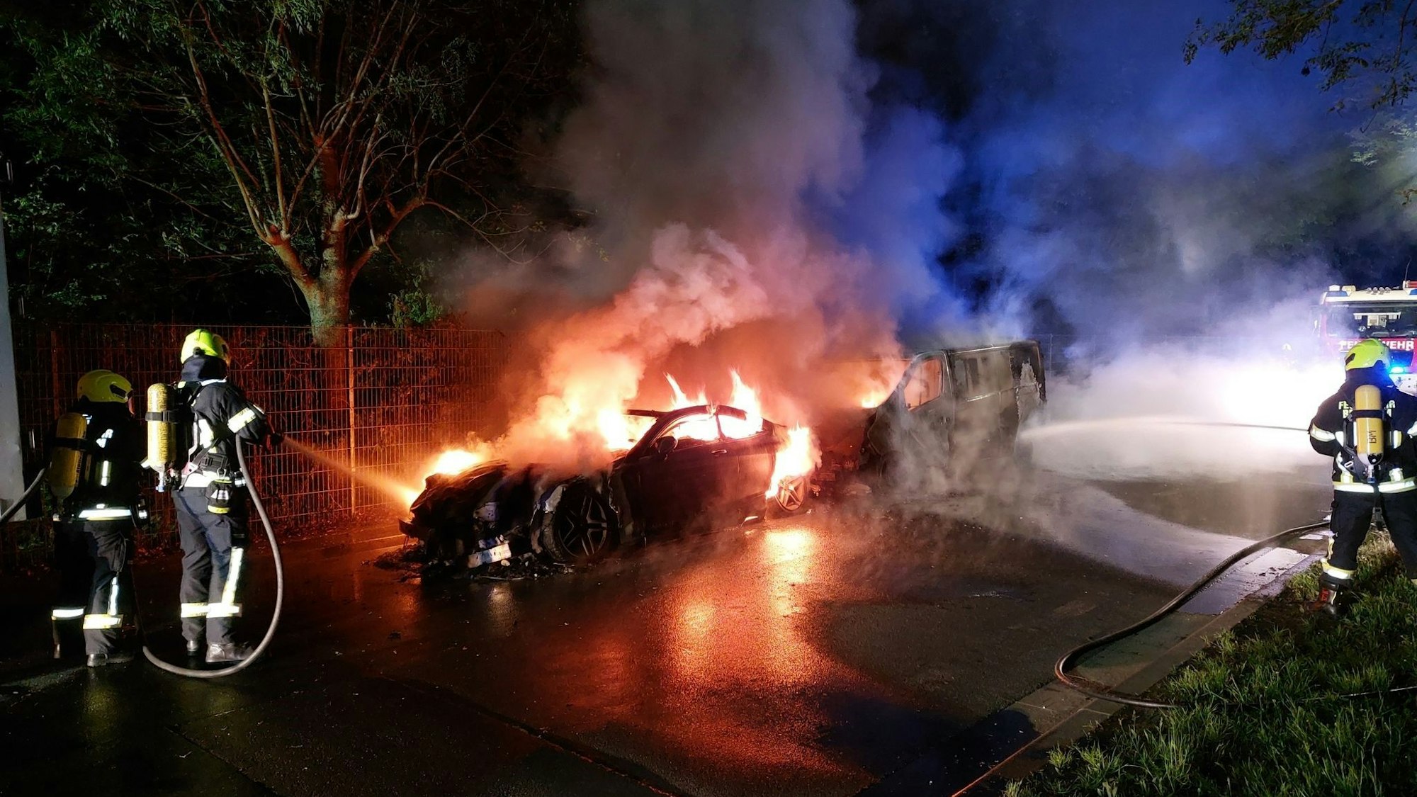 Feuerwehrleute löschen zwei brennende Fahrzeuge in der Nacht.