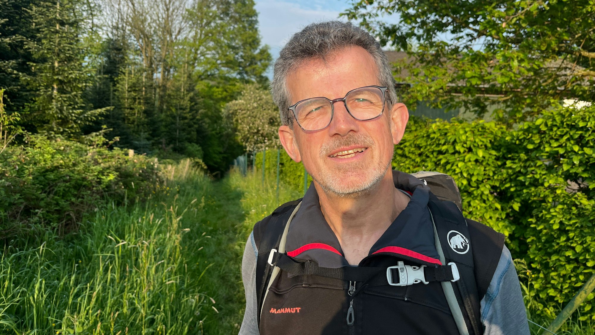 Hans-Peter Sperber steht vor einer Waldkulisse bei Hennef-Niederhalberg im Sonnenschein.