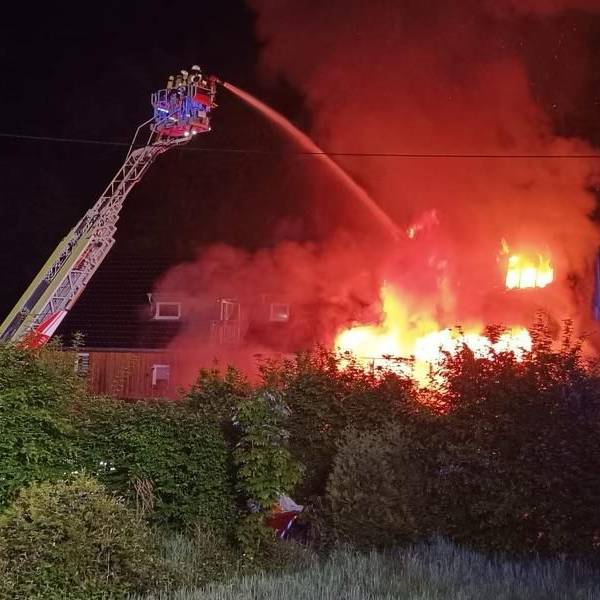 Die Feuerwehr löscht von einer Drehleiter aus ein in Flammen stehendes Haus.