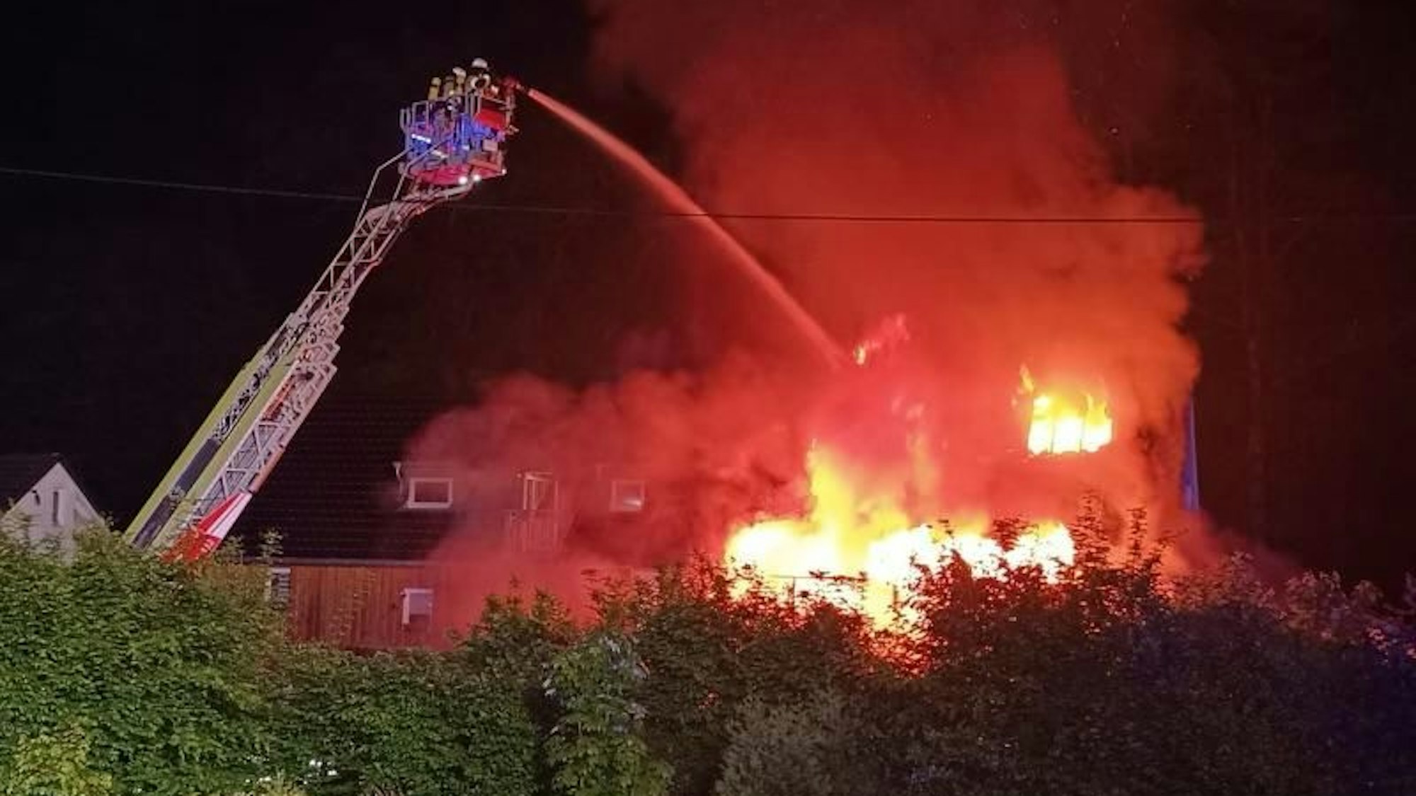 Die Feuerwehr löscht von einer Drehleiter aus ein in Flammen stehendes Haus.