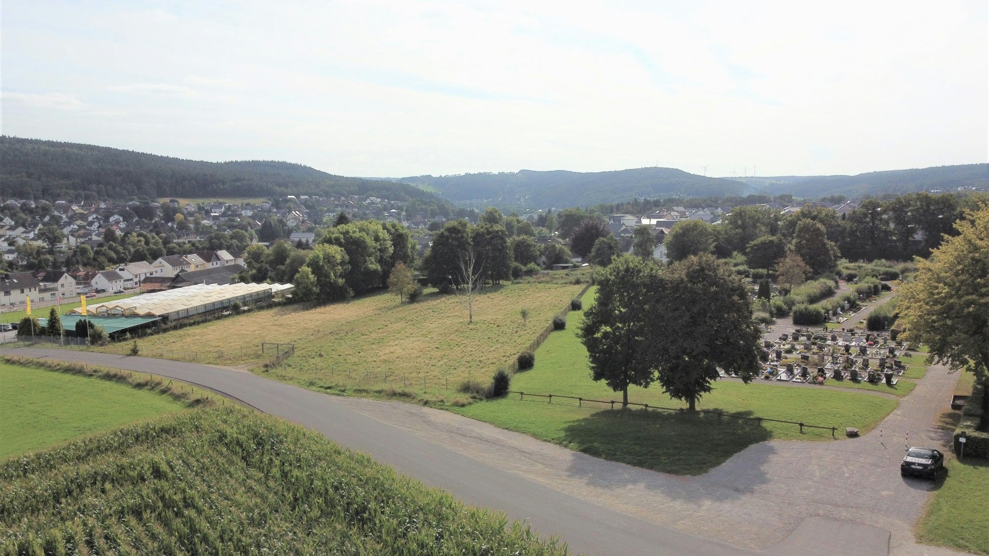 Das Luftbild zeigt die Wiese, auf der das neue Feuerwehrgerätehaus in Kall gebaut werden soll. Links daneben sind die Gewächshäuser einer Gärtnerei zu sehen, rechts davon der Friedhof.
