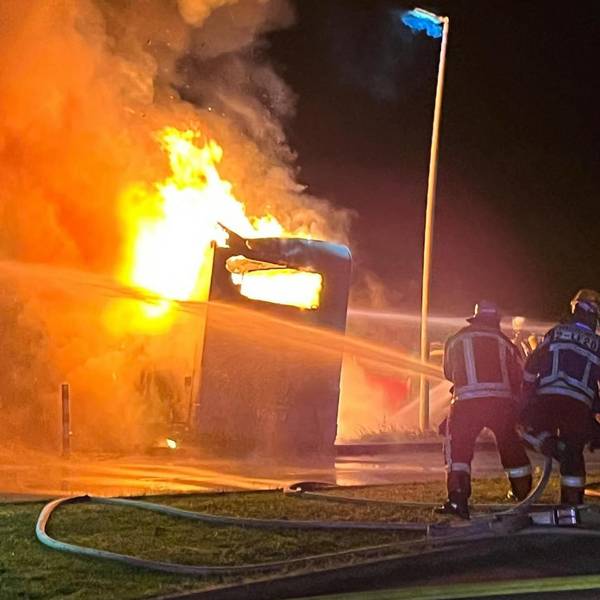 Zwei Feuerwehrleute löschen ein brennendes Wohnmobil.