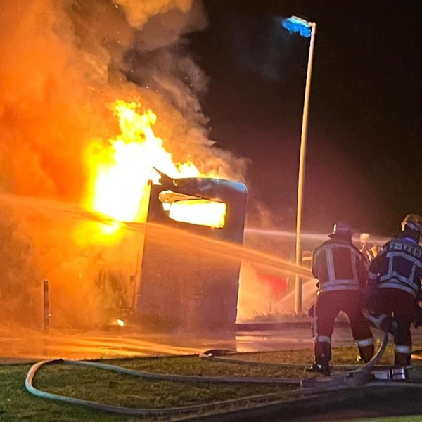 Zwei Feuerwehrleute löschen ein brennendes Wohnmobil.