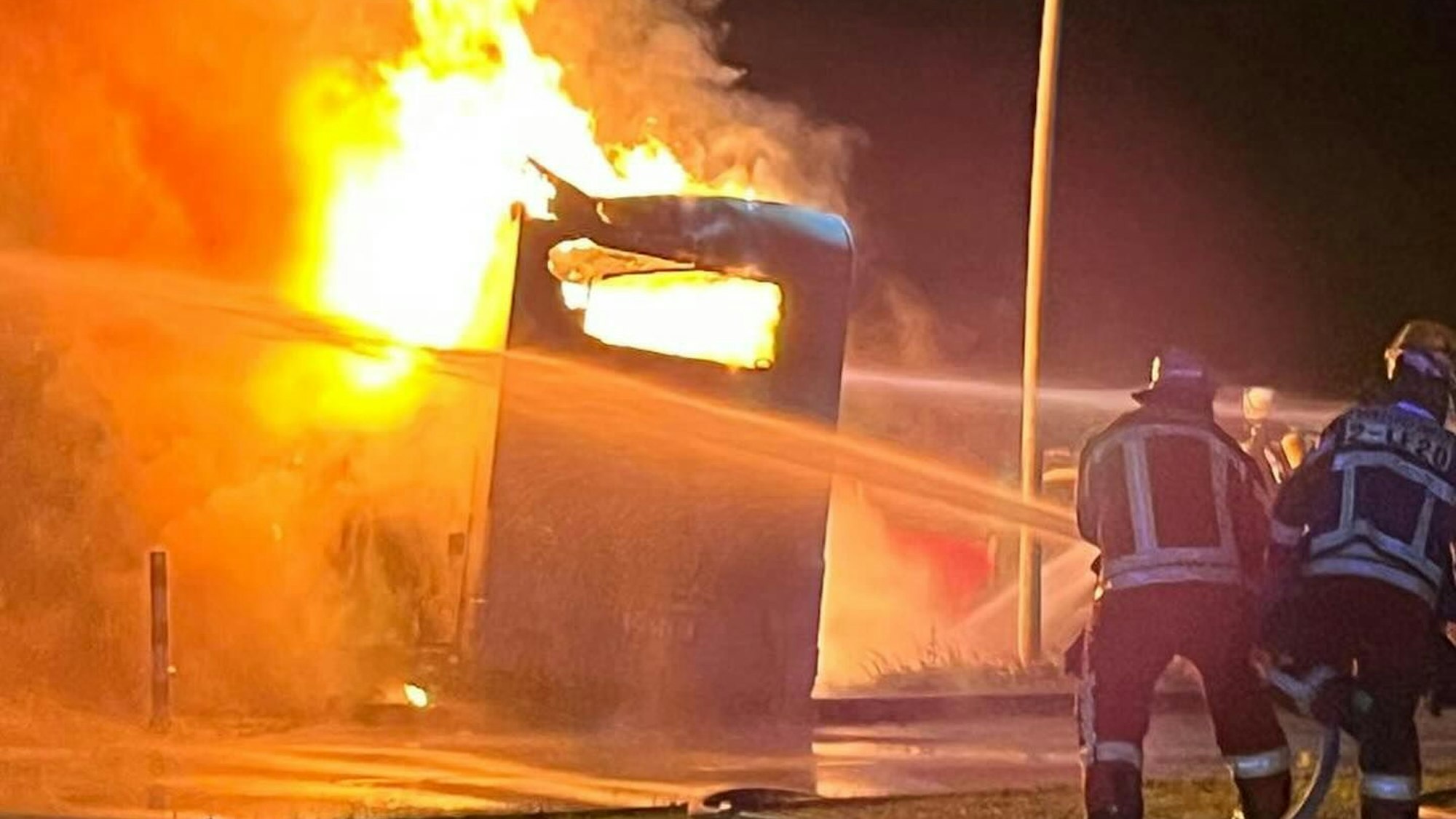 Zwei Feuerwehrleute löschen ein brennendes Wohnmobil.