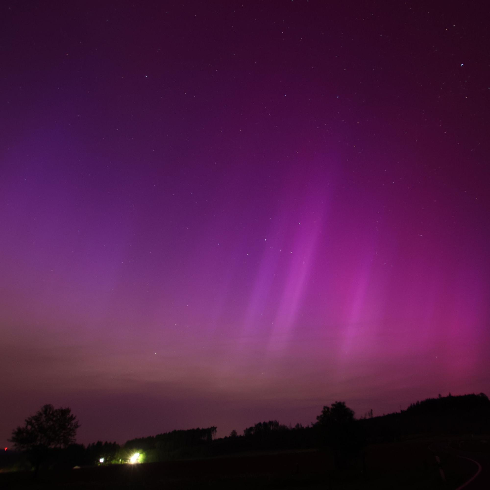 Ein Bild zeigt den in lila, gelb und weiß leuchtenden Nachthimmel als Ergebnis eines Sonnensturms.