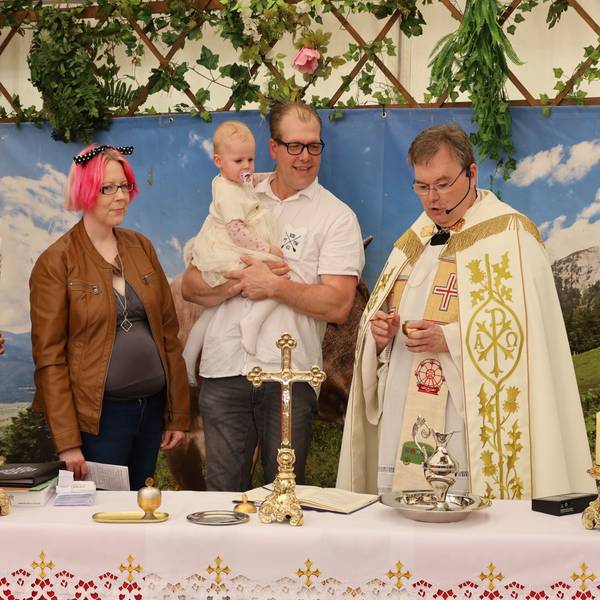 Zwei Männer und zwei Frauen stehen neben einem Pfarrer im Priestergewand. Ein Mann hält seine kleine Tochter auf dem Arm, die in dem Festzelt auf der Euskirchener Kirmes getauft wird