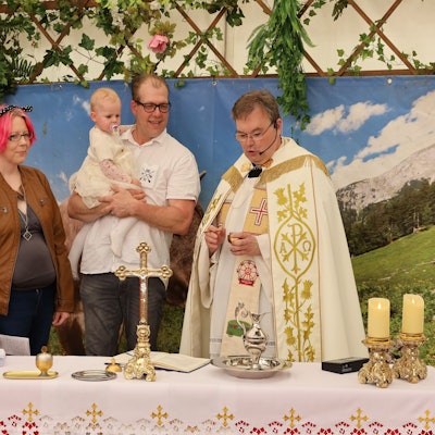 Zwei Männer und zwei Frauen stehen neben einem Pfarrer im Priestergewand. Ein Mann hält seine kleine Tochter auf dem Arm, die in dem Festzelt auf der Euskirchener Kirmes getauft wird