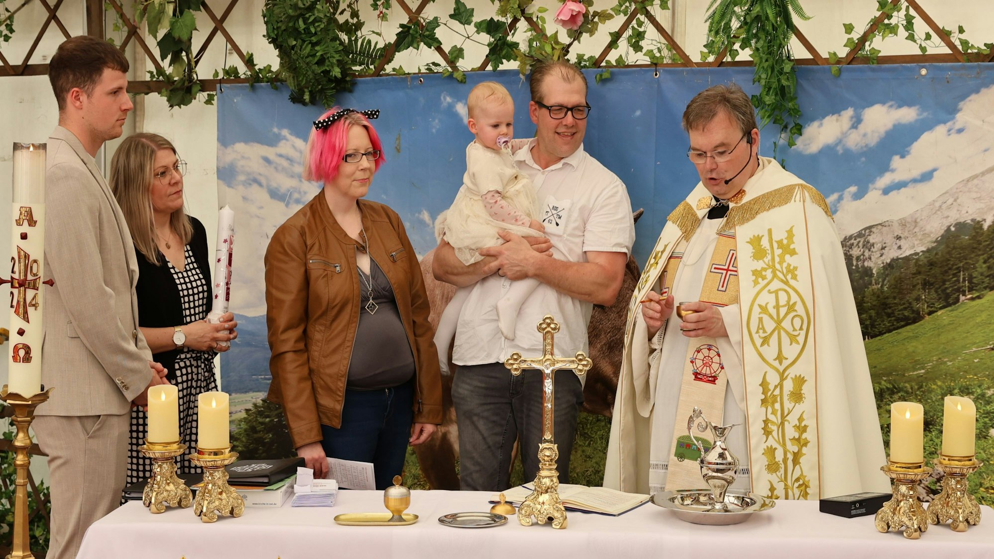 Zwei Männer und zwei Frauen stehen neben einem Pfarrer im Priestergewand. Ein Mann hält seine kleine Tochter auf dem Arm, die in dem Festzelt auf der Euskirchener Kirmes getauft wird