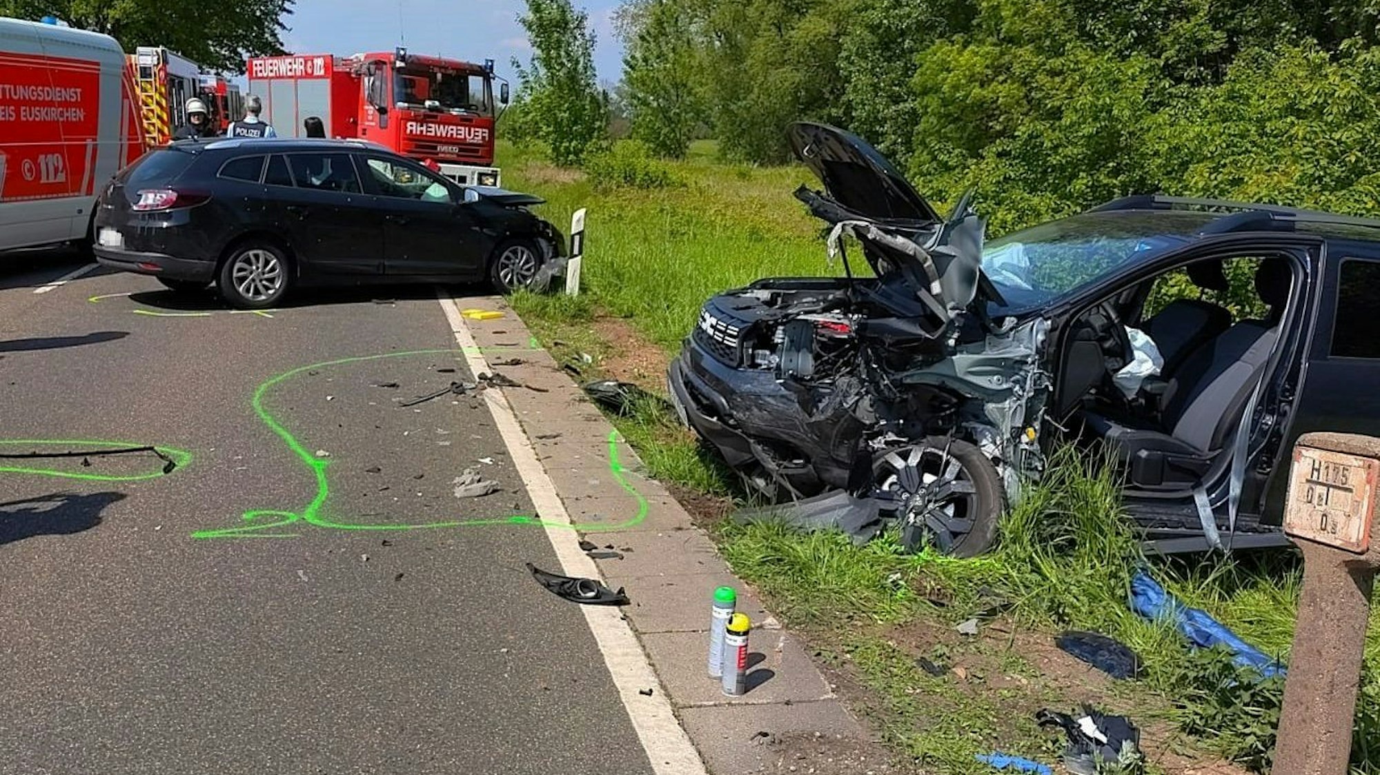 Blick auf die beiden zerstörten Autos. Im Hintergrund sind Feuerwehr und Rettungsdienst zu sehen.
