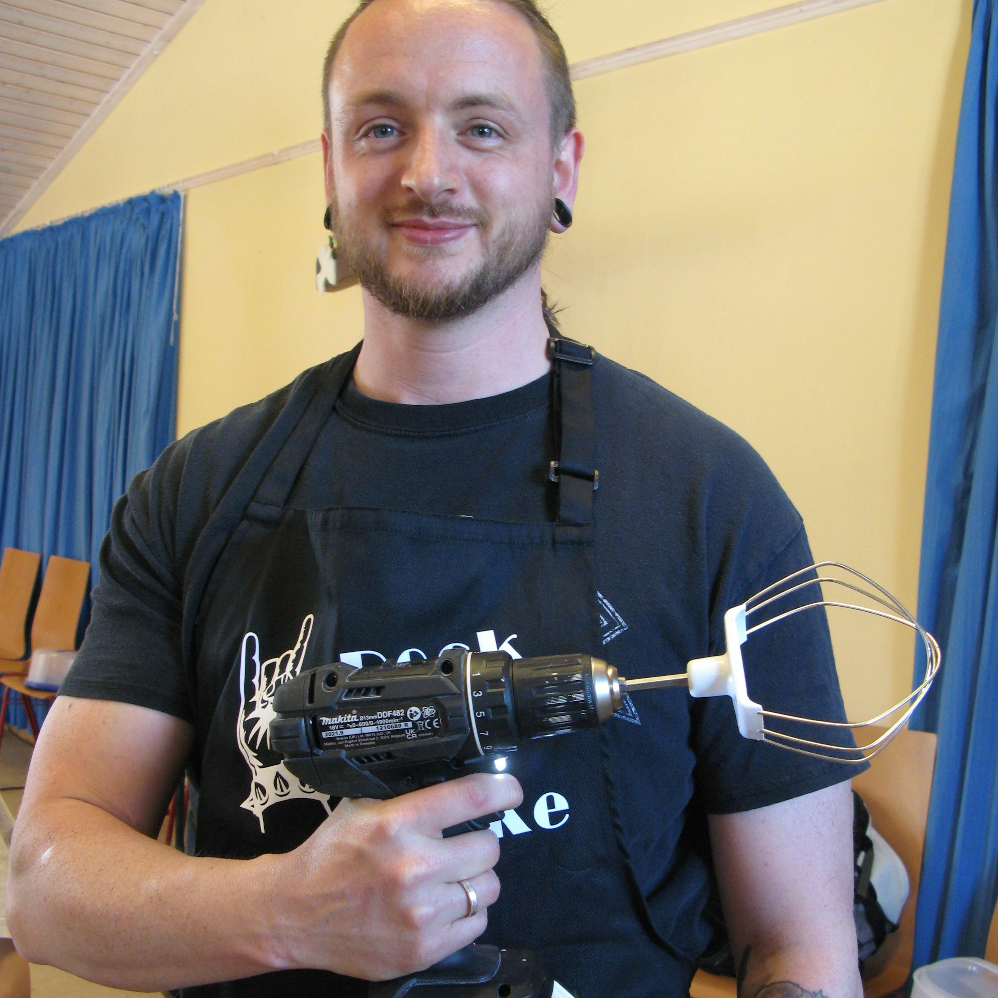 Ein Mann hält einen Akkuschrauber, der Aufsatz ist ein Teigrührer.