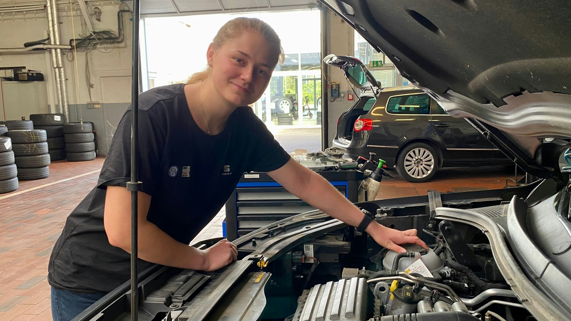Eine junge Frau an einer geöffneten Motorhaube.
