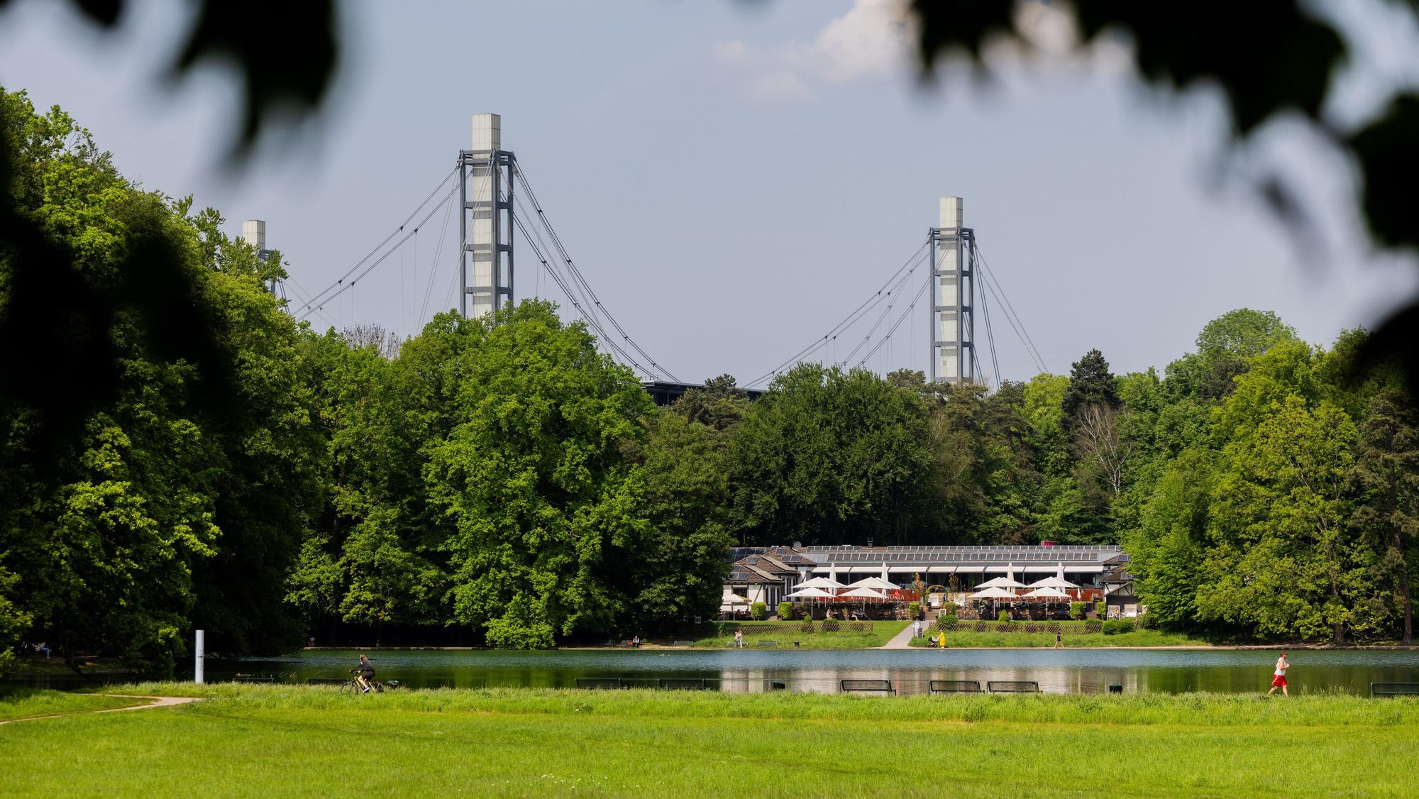 ARCHIV - 02.05.2024, Nordrhein-Westfalen, Köln: Menschen genießen das sonnige Wetter am Adenauer Weiher im Stadtwald vor der Kulisse des RheinEnergieStadions.