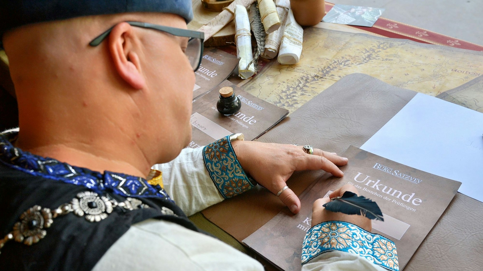 Ein Mann in mittelalterlichem Gewand schreibt mit einer Feder auf einer Urkunde