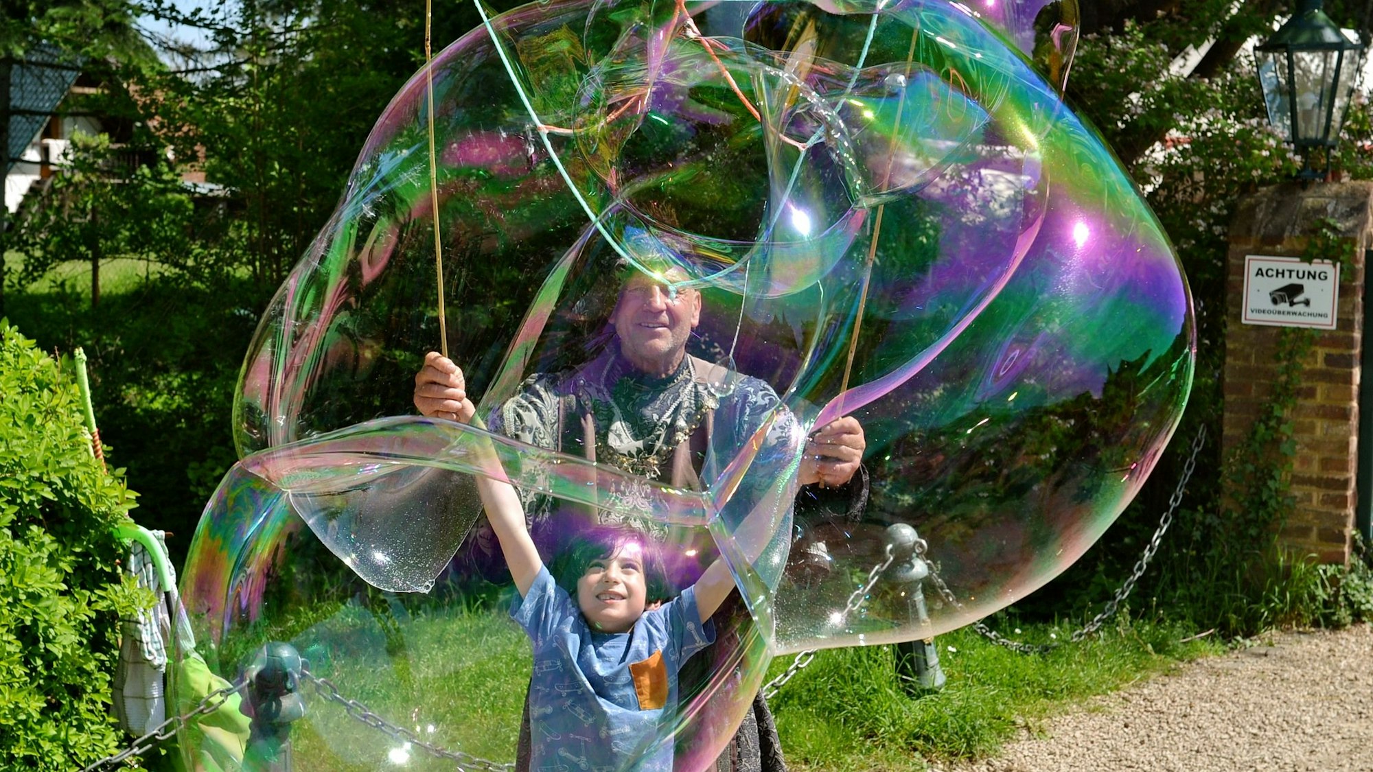 Alfred Schönfelder, der Seifenblasenmann, steht hinter einem Kind, das riesige Seifenblasen erzeugt.