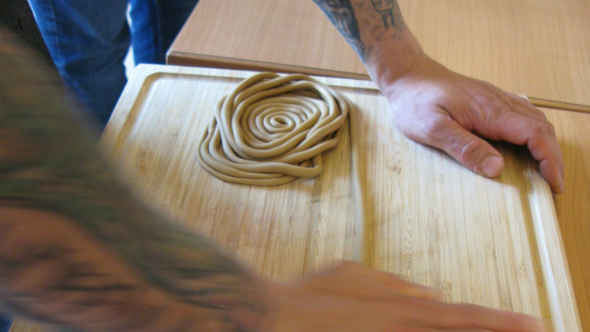 Zwei Hände auf einem Holzbrett modellieren eine braune Zuckermasse.