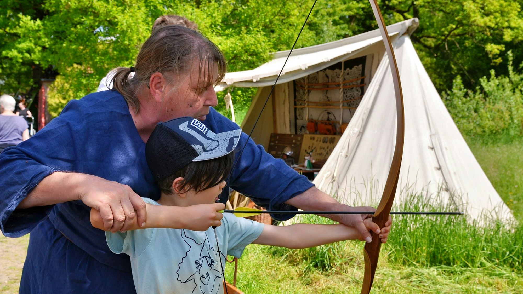 Eine Frau übt mit einem Kind Bogenschießen.