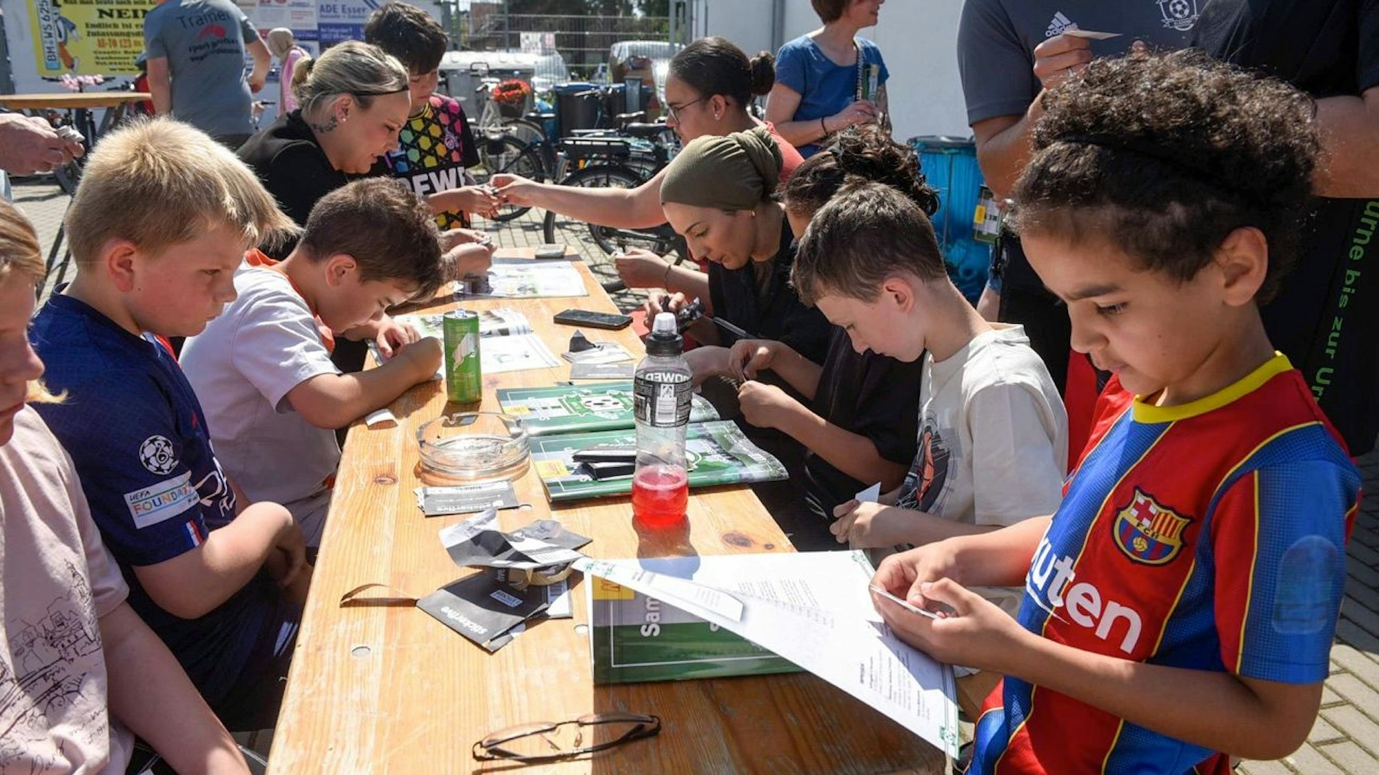 Kinder und Erwachsene sitzen an einem Tisch und kleben die ersten Bilder in das Sammelalbum.