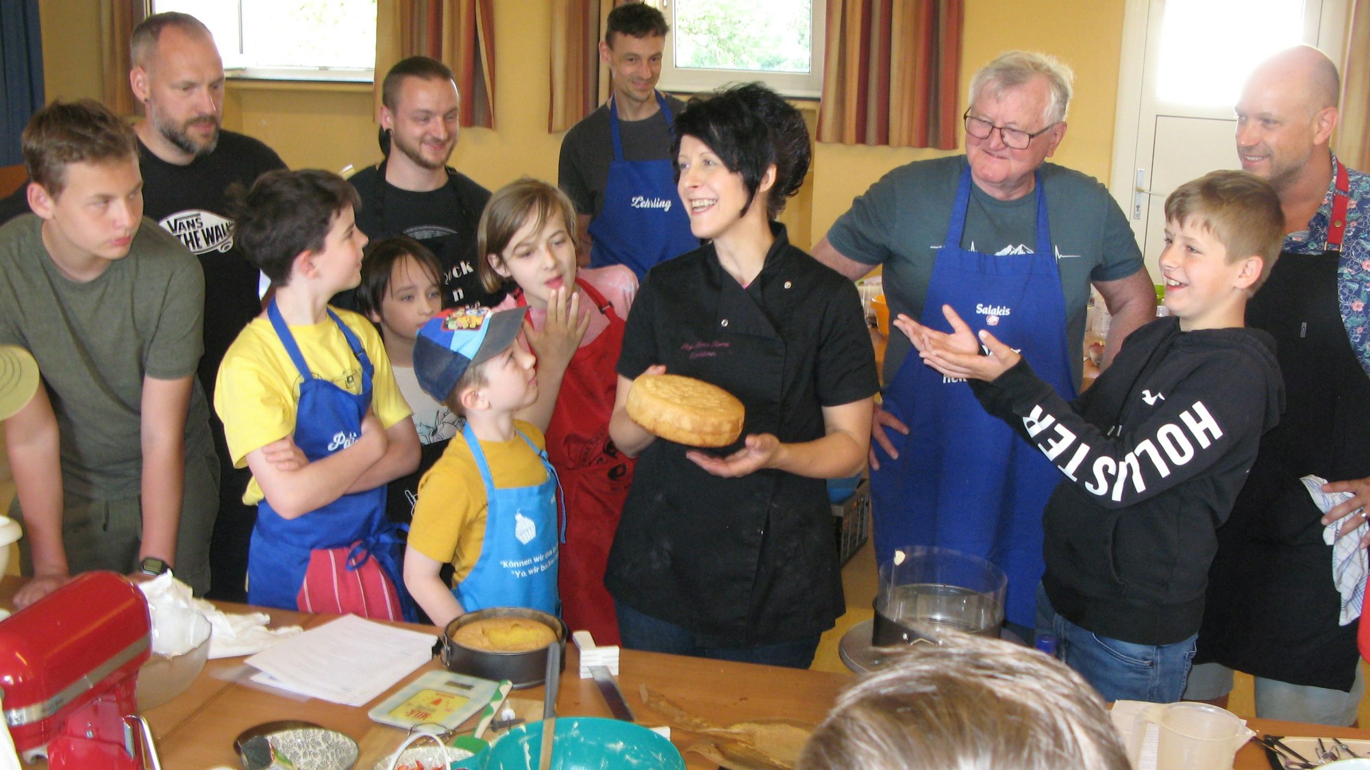 Die Konditorin Anja Rump mit einem Kuchen in der Hand, umringt von Väter und Söhnen im Backkurs.