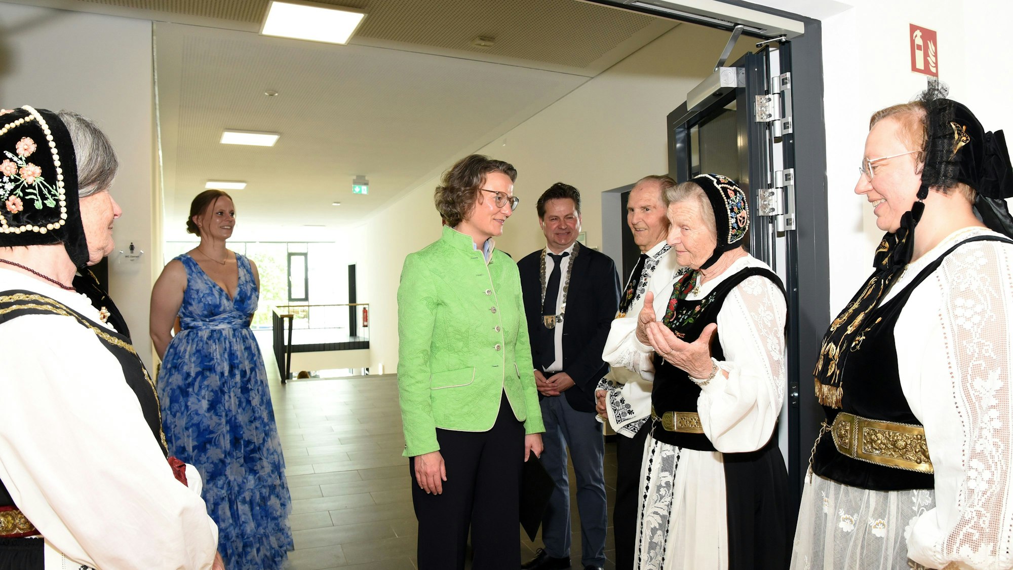 Frauen in der Tracht der Siebenbürger Sachsen begrüßen NRW-Städtebauministerin Ina Scharrenbach an einer Türe.