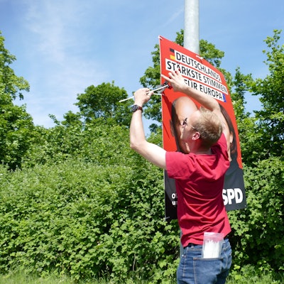 Michael Richter, der Kreisgeschäftsführer der SPD in Bonn und dem Rhein-Sieg-Kreis, hängt an einem Laternenmast ein Plakat zur Europawahl auf.