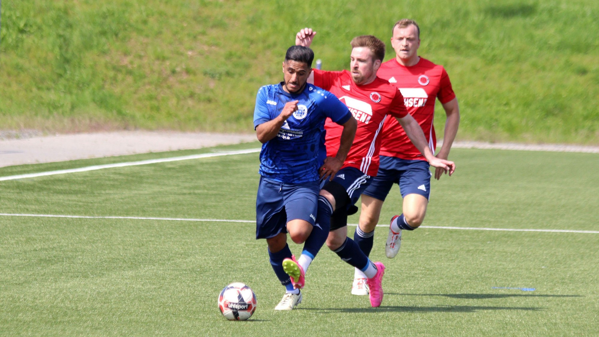 Ein Fußballer läuft mit dem Ball am Fuß, ein Gegenspieler tritt ihm seitlich in die Beine.