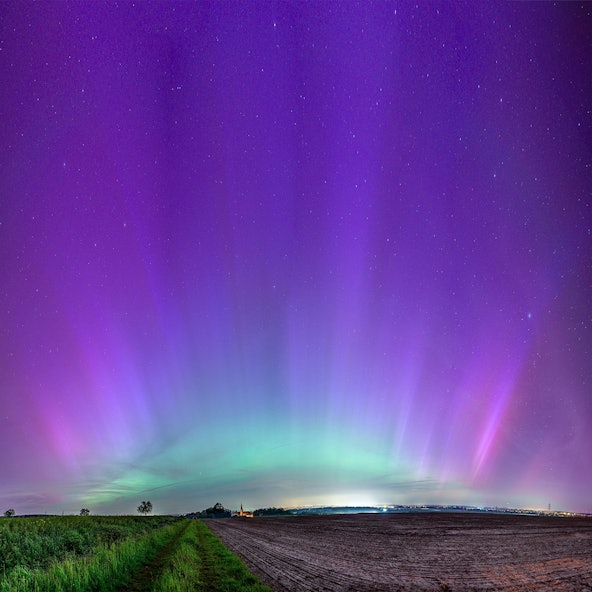 Über einem Feld und einem Kirchturm schillert der Himmel grün und violett.